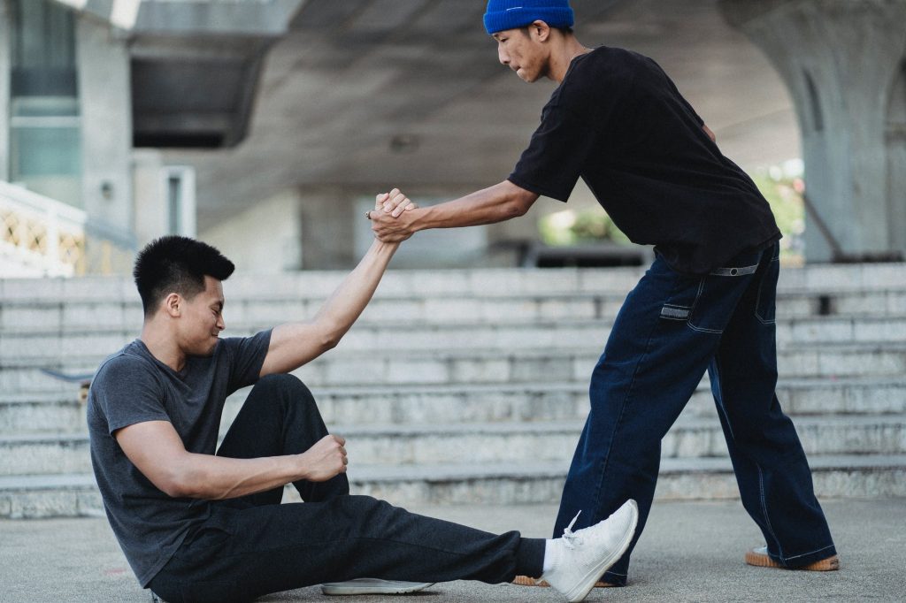 asian man helping friend to get up from ground