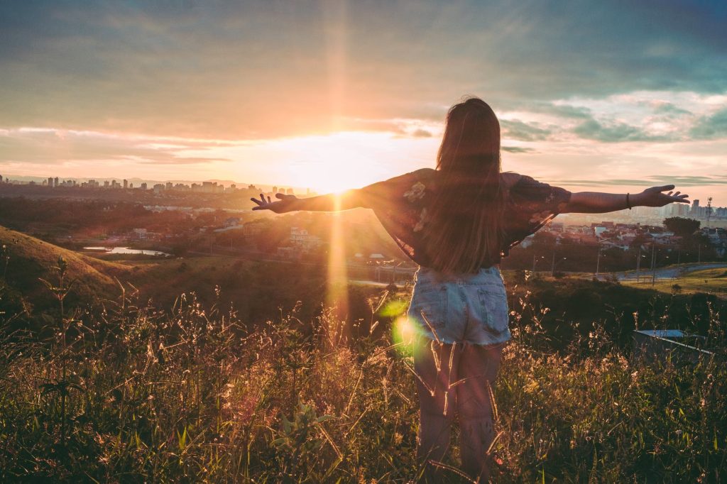 woman stands on mountain over field under cloudy sky at sunrise