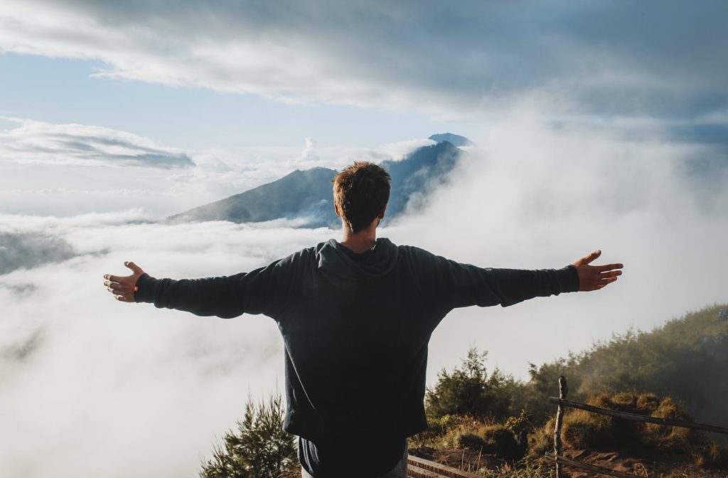 man with arms outstretched admiring view from mountain cliff