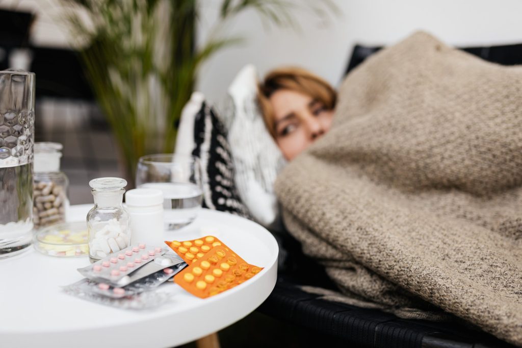 various medicines on a center table beside a woman covered with a blanket