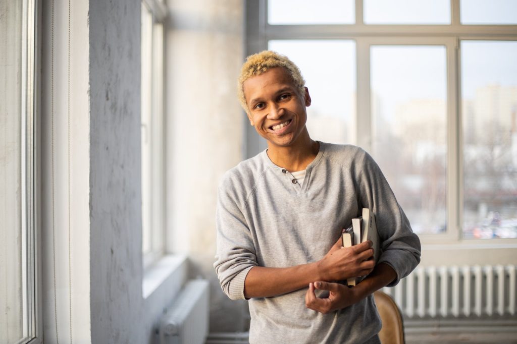 smiling black man standing with books in hand in light studio